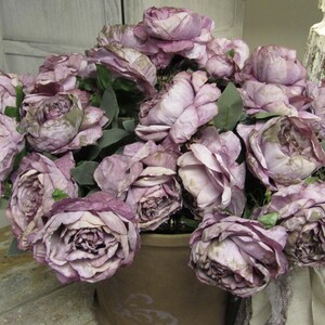 May include: A bouquet of dusty rose silk flowers arranged in a brown ceramic pot. The flowers are in full bloom and have a vintage aesthetic.