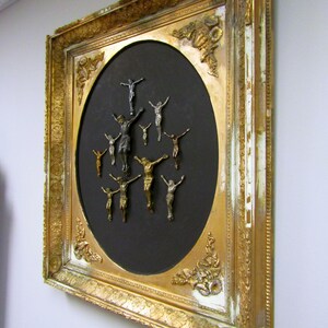 Puede incluir: Un espejo ovalado con marco dorado y fondo negro, que presenta una disposici&oacute;n circular de peque&ntilde;os crucifijos de plata y oro.