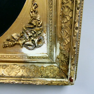 Puede incluir: Primer plano de un marco de imagen dorado con tallas ornamentadas y un acabado de pintura blanca astillada. El marco est&aacute; hecho de madera y tiene un aspecto desgastado.