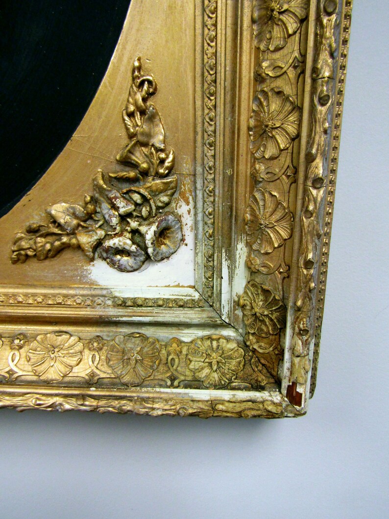 Puede incluir: Primer plano de un marco de imagen dorado con tallas ornamentadas y un acabado de pintura blanca astillada. El marco est&aacute; hecho de madera y tiene un aspecto desgastado.