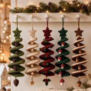Könnte beinhalten: Fünf spiralförmige Häkel-Weihnachtsbaumschmuckstücke hängen an einer weißen Holzleiste. Die Bäume sind grün mit Tannenzapfen, cremefarben mit Sternen, rot mit Beeren, dunkelgrün mit Pilzen und braun mit Eicheln, jeweils mit einem Stern an der Spitze.