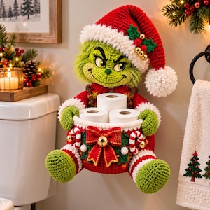Puede incluir: Un soporte para papel higiénico de ganchillo inspirado en el Grinch, con un personaje verde que lleva un gorro de Papá Noel rojo con un pompón blanco. La figura sostiene una cesta roja decorada con un gran lazo, un cascabel dorado y bastones de caramelo.