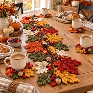 Peut inclure: Un chemin de table et des dessous de verre en crochet ornés de feuilles d'automne rouges, orange, jaunes, crème et vertes, agrémentés de petits glands et baies en crochet, disposés sur une table en bois avec des tasses et des bols.