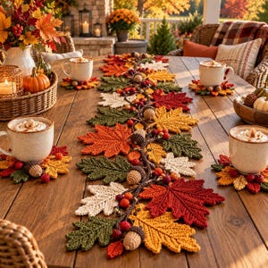 Pode incluir: Um caminho de mesa e porta-copos de crochê com um padrão de folhas de outono em tons de vermelho, laranja, amarelo, verde e creme, acentuado com pequenas bolotas e bagas de crochê, dispostos numa mesa de madeira com canecas de bebidas quentes.