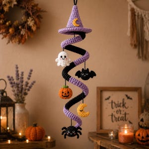 May include: A hanging crochet spiral decoration featuring a purple witch hat with a yellow crescent moon at the top. The spiral alternates between purple and black yarn, adorned with small crocheted figures: a white ghost, a black bat, an orange pumpkin, a yellow crescent moon, and a black spider.