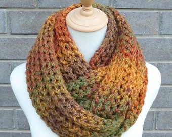 May include: A chunky knit infinity scarf featuring a variegated yarn pattern with blended tones of burnt orange, deep brown, forest green, and golden yellow. The scarf has a thick, open-stitch texture and is displayed on a neutral mannequin form.