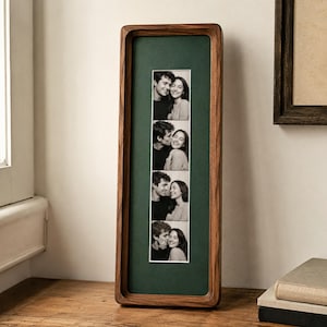 May include: A tall, rectangular wooden picture frame with a dark walnut finish, featuring a deep green mat board. The frame holds a vertical strip of four black and white photographs showing a couple in various affectionate poses.
