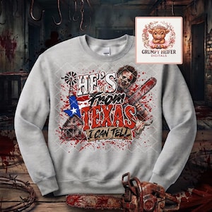 May include: A light gray crewneck sweatshirt featuring a graphic print with the text HE'S FROM TEXAS I CAN TELL. The design includes a horror character holding a chainsaw, a Texas state shape, a windmill, a house, and a cow skull with red splatters.