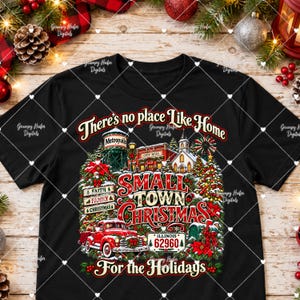 May include: A black t-shirt featuring a graphic print with the text "There's no place Like Home", "SMALL TOWN CHRISTMAS", and "For the Holidays". The design includes a red truck, a water tower labeled "Metropolis", a city hall, and a sign reading "ILLINOIS 62960".