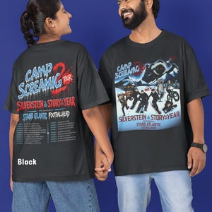 May include: A black short-sleeved t-shirt featuring a graphic print for the Camp Screaming 2 Tour. The front displays a winter-themed illustration with band names Silverstein and Story of the Year. The back lists tour dates and locations.