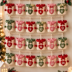 May include: A wall-hanging advent calendar featuring twenty-four small, cream-colored crocheted pouches suspended from a wooden rod. Each pouch displays a red or green heart with a white number from 1 to 24, accented with bows.