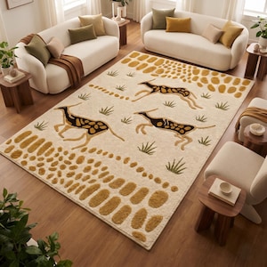 Op de afbeelding: Een rechthoekig vloerkleed met een crèmekleurige achtergrond en een herhalend patroon van drie springende gazellen in donkerbruin en beige, afgewisseld met kleine groene getufte grasmotieven en randen van getextureerde mosterdgele ovalen.