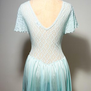 May include: A light blue dress featuring a V-neckline and short flutter sleeves. The bodice is constructed from a delicate floral lace overlay, while the lower portion of the dress consists of a smooth, solid-colored fabric with a gathered waistline.