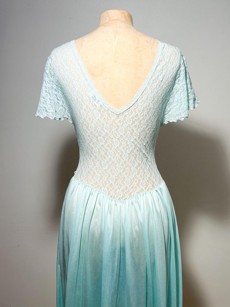 May include: A light blue dress featuring a V-neckline and short flutter sleeves. The bodice is constructed from a delicate floral lace overlay, while the lower portion of the dress consists of a smooth, solid-colored fabric with a gathered waistline.