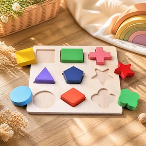 Puede incluir: Un tablero de rompecabezas de madera con nueve huecos para encajar formas. El conjunto incluye un cuadrado amarillo, un rectángulo verde, una cruz rosa, un triángulo morado, un pentágono azul, una estrella roja, un círculo azul claro, un rombo naranja y un bloque con forma de trébol verde.