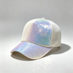 Op de afbeelding: Een baseballpet met een voorpaneel en gebogen klep bedekt met iriserende, lichtreflecterende lovertjes die verschuiven tussen witte, blauwe en paarse tinten. De achter- en zijpanelen zijn gemaakt van witte mesh-stof met een knoop bovenop.