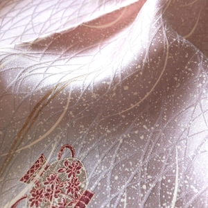 May include: A light pink fabric featuring a repeating pattern of white curved lines and white speckles. The textile includes a decorative motif of a small, ornate vessel in shades of red, white, and gold, integrated into the overall design.