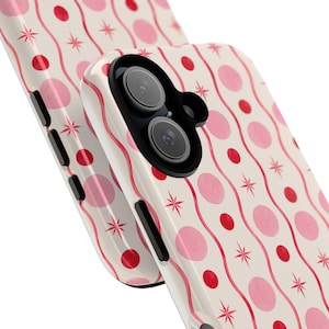 May include: A cream-colored phone case featuring a repeating pattern of vertical wavy red lines, light pink circles, and small red starburst shapes. The case has a black camera cutout and black side buttons, shown from an angled perspective.