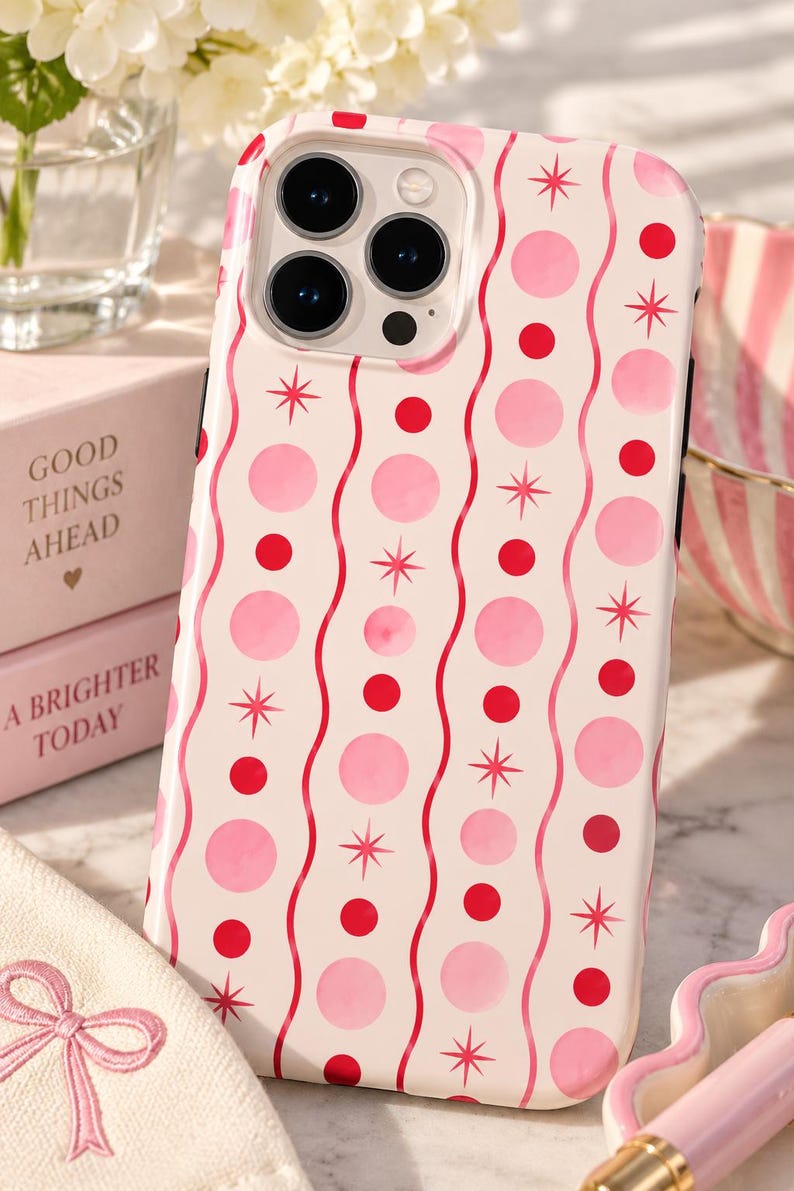 May include: A phone case with a cream background featuring a repeating pattern of vertical wavy pink lines, alternating solid red circles, light pink circles, and small red starburst icons. The case has a cutout for a triple camera lens system.