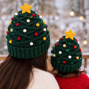 Könnte beinhalten: Zwei dunkelgrüne Häkelmützen in Form von Weihnachtsbäumen, die jeweils mit einem gelben Häkelstern gekrönt sind. Die Mützen haben einen gerippten Rand und sind mit kleinen, bunten Pompons in Rot, Weiß und Gelb über die Oberfläche verziert.
