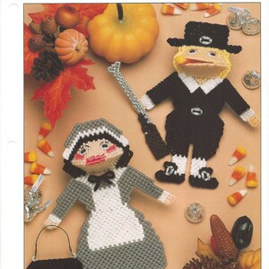 May include: A plastic canvas craft pattern for a pilgrim couple. The woman is holding a black bucket and the man is holding a gun. The pattern is titled "Pilgrim Kisses" and is designed by Arlene Engeriser.