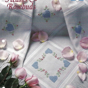 May include: Cross stitch pattern for a white tablecloth with blue hearts and pink rosebuds. The pattern is titled "Hearts & Rosebuds" and is part of the "Cross Stitch Collector's Series".