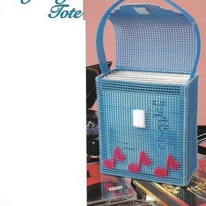 May include: A blue plastic canvas tote bag with a pink musical note design. The tote is designed to hold CDs and has a flap that opens to reveal the inside. The tote is sitting on top of a stack of CDs. The image includes the text "Jazzy CD Tote" and "Quick Stitching".