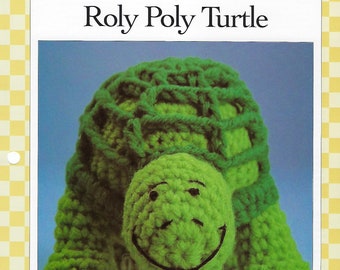 May include: A green crocheted turtle toy with a smiling face. The turtle is designed to be a roly poly toy.