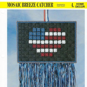 May include: A mosaic breeze catcher in the shape of a heart with red, white, and blue squares. The heart is surrounded by a black border and has a fringe of blue and black yarn hanging from the bottom.