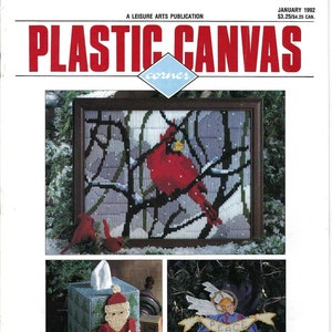 May include: A magazine cover for Plastic Canvas Corner, a leisure arts publication. The cover features three plastic canvas projects: a cardinal in a snowy forest, a tissue box cover with a Santa Claus design, and a Christmas angel holding a banner that says "Peace". The magazine cover is from January 1992.