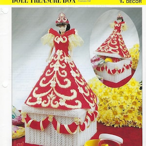 May include: A white plastic canvas box decorated with red and gold embroidery, shaped like a doll wearing a red and gold dress. The box is open and the inside is visible. The doll is wearing a crown and has a yellow and white lace trim on her sleeves. The box is surrounded by yellow flowers and red and white ribbon.