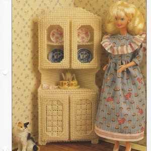 May include: A cream-colored corner cabinet with a doll and a cat figurine. The cabinet has two glass-doored shelves with decorative plates and a lower cabinet. The doll wears a blue dress with a rooster pattern. The text "CORNER CABINET" is at the top.