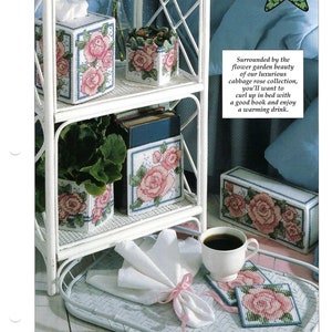 May include: A display of home decor items featuring a cabbage rose design. The items include a tissue box, planters, a book holder, coasters, and a rectangular box. The items are white with pink and green floral patterns and blue accents. The text "Cabbage Roses" is at the top.