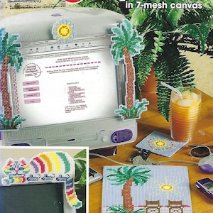 May include: A computer screen with a plastic canvas pattern of a palm tree on the screen. The computer is on a desk with a glass of iced tea, a pair of sunglasses, a cell phone, and a mouse. There is also a plastic canvas pattern of a cat and a palm tree on the desk.