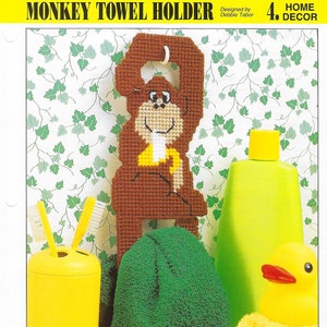 May include: A brown monkey towel holder with a yellow banana in its hand. The monkey is holding a towel ring. The monkey is on a green and white background. HOME DECOR 4.