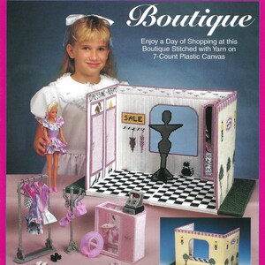 May include: A pink and white plastic canvas doll boutique set with the text "Fashion Doll Carry & Play Boutique". The set includes a dressing room, clothing racks, and accessories. The set is designed to be stitched with yarn.