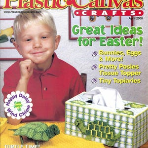 May include: The cover of a craft magazine, "Plastic Canvas Crafts," features a young boy and a tissue box with a turtle design. The magazine promotes Easter-themed craft ideas, including bunnies, eggs, and tissue toppers. The magazine is dated April 2000.