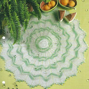 May include: A white and green crochet doily with a starburst pattern. The doily is called "Starburst Centerpiece" and is part of the "Twinkling Stars" collection.