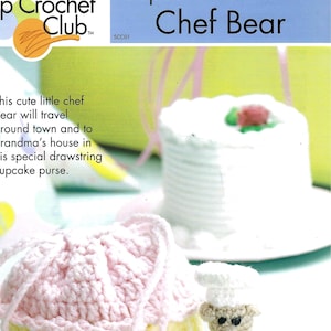 May include: A crocheted cupcake purse with a pink frosting and yellow cupcake base. A small crocheted chef bear with a white hat and apron is standing next to the purse. The text "For the Little Ones Cupcake Purse With Chef Bear" is printed on the left side of the image.