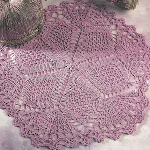 May include: A pink crocheted doily with a delicate, intricate design. The doily is called "Grandmother's Ceiling Fan" and is part of a collection of heirloom table toppers.