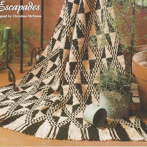 May include: A black and cream checkered crochet afghan with fringe. The afghan is draped over a black metal stand and a potted plant is in the foreground. The text "Checkered Escapades" is at the top of the image.
