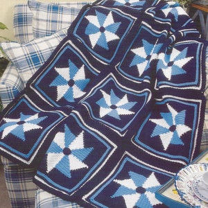 May include: A crochet blanket with a blue, white, and gray pinwheel pattern. The blanket is draped over a plaid couch.