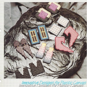 May include: A book cover featuring various plastic canvas earring designs. The title reads "Plastic Canvas 14-Count Earrings" with the "Nifty Publishing Company" logo. The cover displays several colorful, handmade earring examples.