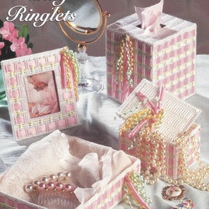 May include: A set of four pink and white plastic canvas boxes with ribbon embellishments. The boxes are labeled "Vanity Ringlets" and are part of the "Collector's Series".