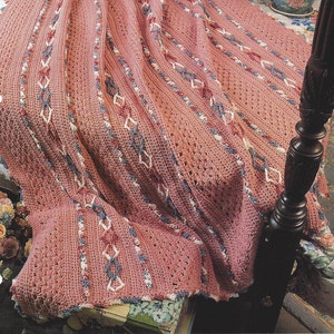 May include: A dusty rose crochet afghan featuring vertical panels of textured cable stitches and diamond-shaped lattice patterns in white, blue, and rose yarn. The text "TRELLIS & CABLES AFGHAN" is printed in white at the top left of the image.