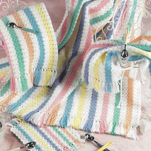 May include: A collection of pastel-colored crocheted items, including blankets and placemats, with striped patterns and fringe. The text "SHELL SELECTIONS" is visible. Serving spoons with white handles are also present.