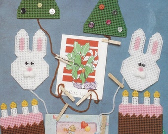 May include: A collection of plastic canvas ornaments, including a Christmas tree, a bunny rabbit, and a birthday cake, are shown hanging from a string. The ornaments are used to decorate cards and create seasonal displays. The text "Seasonal Card Displays" is printed on the page.