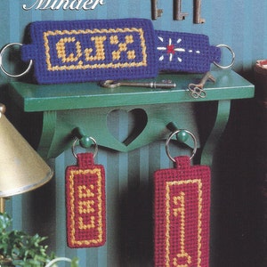 May include: A plastic canvas craft kit for a key minder. The kit includes a blue and yellow key minder with the letters "C.J.H." and two red and yellow key tags, one with the number "1" and the other with a key design. The kit is titled "Just for Me" and is part of the "Collector's Series" of plastic canvas kits.