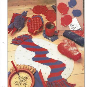 May include: A red and blue plastic canvas pattern for a scarf and mittens. The scarf is a long, narrow rectangle with a fringe on the ends. The mittens are small and round with a pointed tip. The pattern is designed to be worked with plastic canvas and yarn.