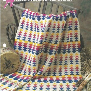 May include: A colorful crochet blanket with a geometric arrowhead pattern in shades of red, yellow, blue, and white. The blanket is draped over a wooden wagon wheel.